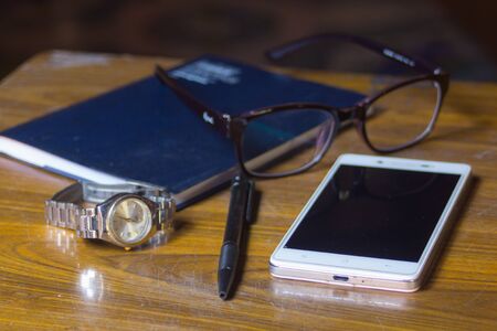 smart-phone watch Glasses  pen and book on wood table for business or education conceptの写真素材