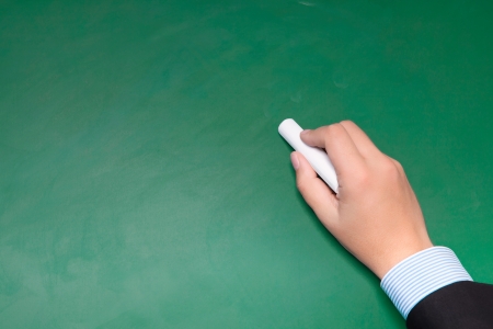 male businessman hand in suit writing on a green blackboard with white chalk の写真素材