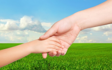 man hand and a child hand holding each other on the background of green field and blue skyの写真素材