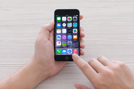 Alushta, Russia - October 23, 2014: man holding new phone iPhone 6 Space Gray over the table. iPhone 6 was created and developed by the Apple inc.のeditorial素材