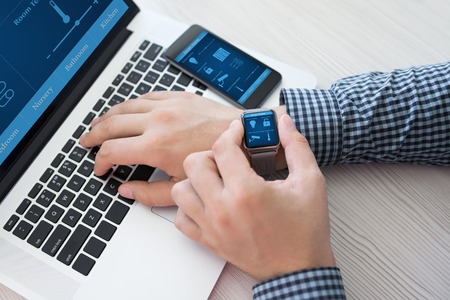 man hand in watch with program smart home on the screen against the background of computer and phone