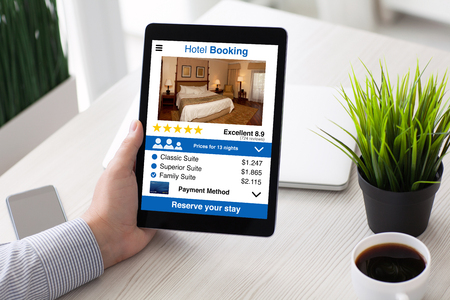 man hand holding computer tablet with app hotel booking screen on table in roomの写真素材