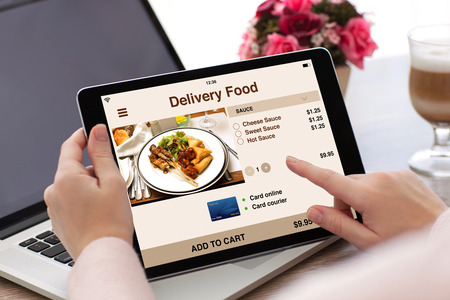 woman hands holding tablet computer with app delivery food on screen and laptop の写真素材