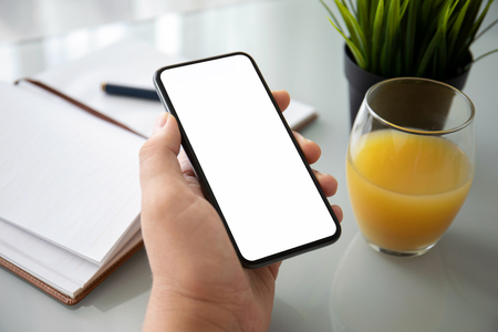 man hand holding phone with isolated screen over table in the officeの写真素材
