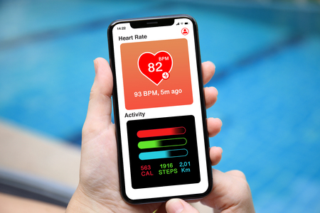 female hands holding phone with app heart and activity screen on background of the poolの写真素材