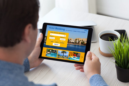 man in office holding tablet computer with app hotel booking on screen