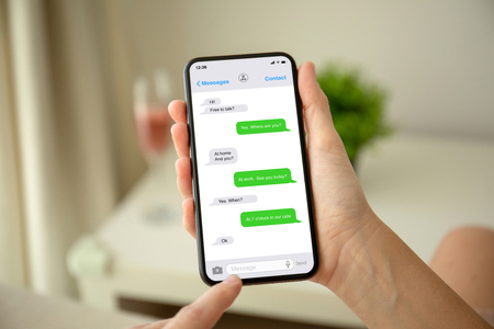 female hands holding phone with app messenger on the screen in the house in roomの写真素材