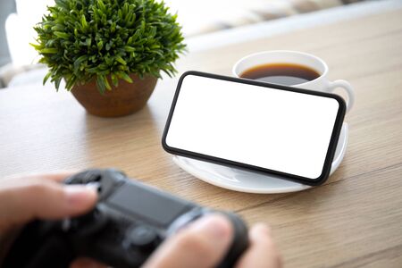 male hands holding joystick over a table and phone with isolated screenの写真素材