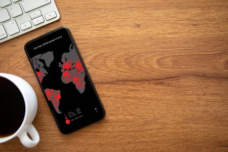 phone with live map global spread of virus on the screen on table with keyboard and cup of coffee in officeの写真素材
