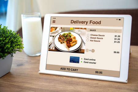 white computer tablet with food delivery application on screen table with glass of milk in cafeの写真素材