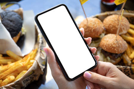 female hands holding phone with isolated screen on background of burgersの写真素材