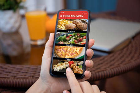female hands hold phone with food delivery application on screen against background of room in houseの写真素材