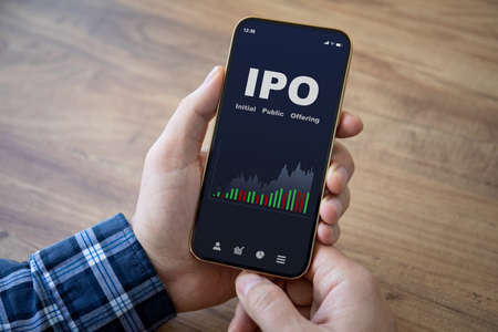 male hands hold phone with IPO stocks purchase app on screen wooden table backgroundの写真素材