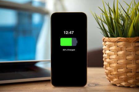 Gold Phone with charged battery on the screen on wooden table in officeの写真素材