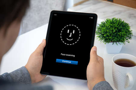 man holding computer tablet with scanning face on screen in the officeの写真素材