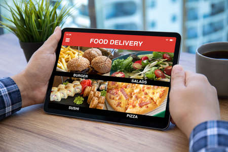 male hands holding computer tablet with app food delivery on screen over table in cafeの写真素材