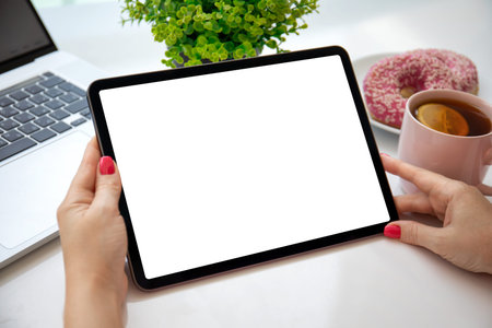 female hands holding computer tablet with isolated screen over table with laptop in cafe