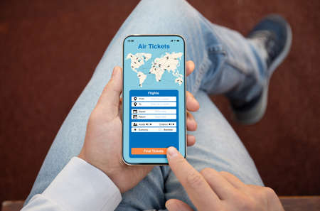 male hands holding phone with application search air tickets on the screen background of jeansの写真素材