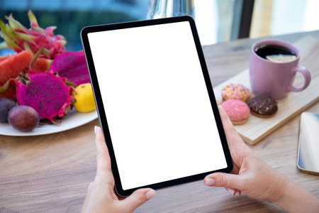 female hands holding computer tablet with isolated screen on table background of fruits in cafe