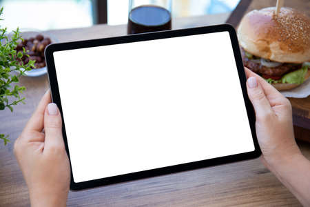 female hands holding computer tablet with isolated screen background burger in cafeの写真素材