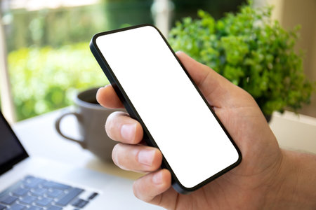 man hand holding phone with isolated screen background of laptop in cafe