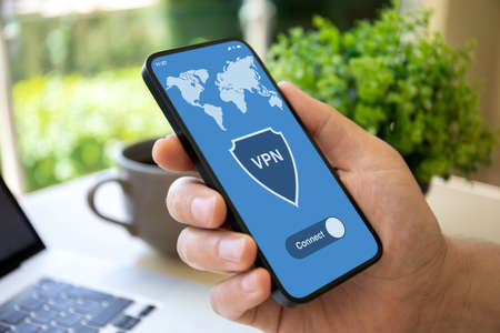 male hand holding phone with app vpn on screen over table with laptop in officeの写真素材