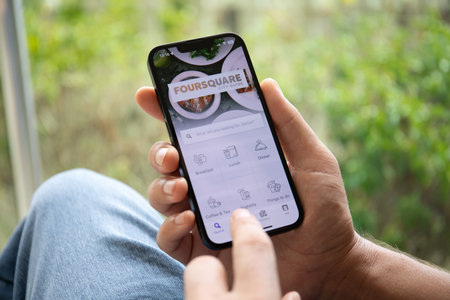 Alanya, Turkey - October 4, 2022: Man hands holding Apple iPhone 14 with social networking service Foursquare on the screen. iPhone 14 was created and developed by the Apple inc.のeditorial素材