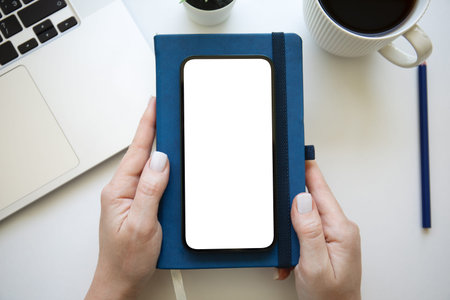 woman hand holding phone with isolated screen background of table with laptop keyboard in office
