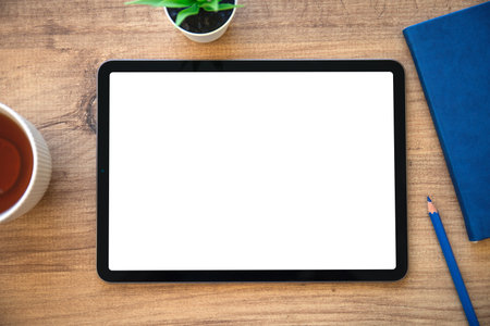 Tablet with isolated screen on wooden table with blue notepad in officeの写真素材