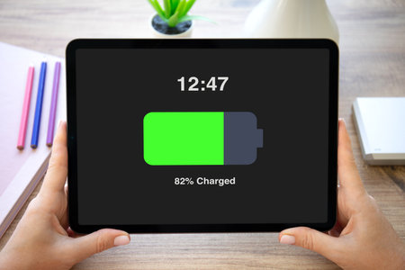 woman hands hold computer tablet with charged battery on screen background of table in officeの写真素材