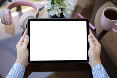 Female hands holding computer tablet with isolated screen on background of table with headphones in officeの写真素材