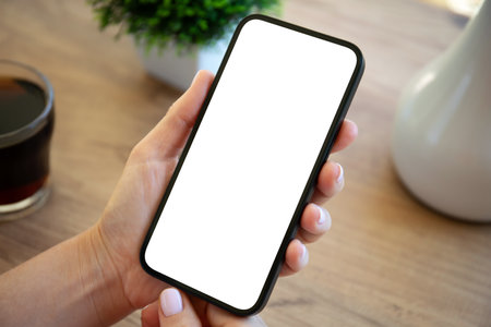 female hands holding phone with isolated screen background of wooden table in apartmentの写真素材