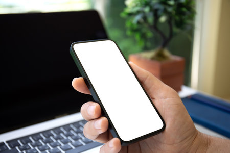 male hand hold phone with isolated screen background laptop in officeの写真素材