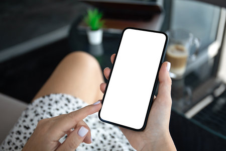 female hands hold phone with isolated screen background of laptop in cafe in officeの写真素材