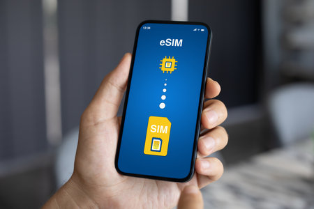 Man hand holding phone with Sim card replacement on eSim on screen in officeの写真素材