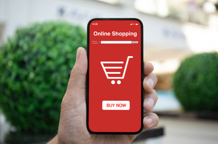 Man hands hold phone with app online shopping on screen background of green streetの写真素材