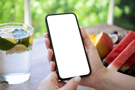 Woman hand hold phone with isolated screen background of table with fruits in cafeの写真素材