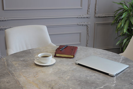 Cup of coffee, diary and laptop on the table in a modern interior