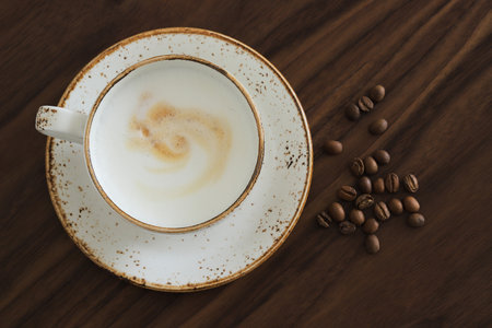 White cup of cappuccino with coffee beans on a brown wooden table, top viewの写真素材