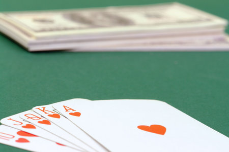 Royal flush cards put on green table cloth with pile of dollars in the background
