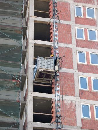 Construction worker using external elevator on raw buildingの写真素材