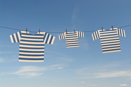 Three white-and blue striped sailor-suits of mom dad and kid drying on washing line over blue sky - summer holiday conceptの写真素材