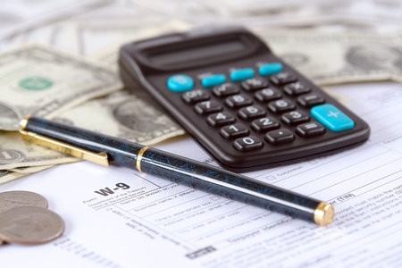Blank W-9 income tax form with pen, calculator and american dollars