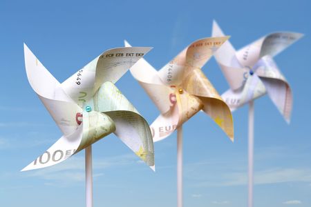 Three toy windmills cut from 100, 50 and 20 euro banknotes over blue skyの写真素材