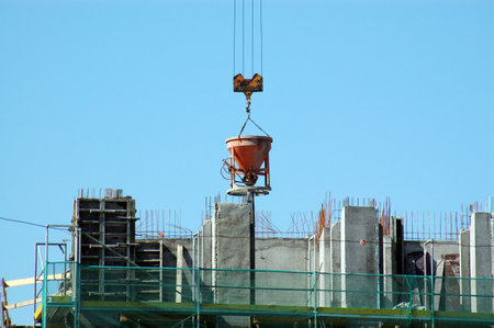 Charging hopper with concrete mix being transported by jib crane at the construction site