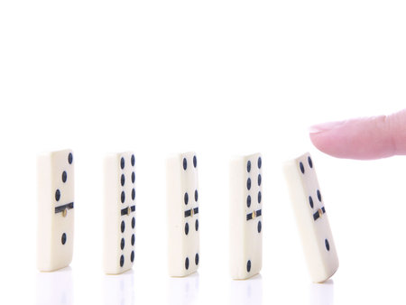 Finger pushing first domino piece in a row over white