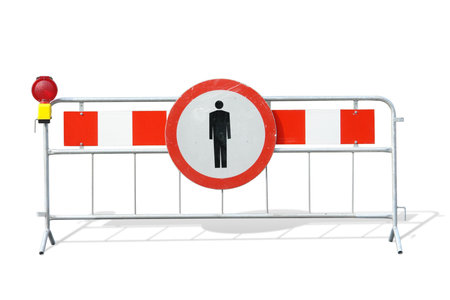 Metal red and white striped road construction barrier with no access sign and red beacon over white backgroundの写真素材