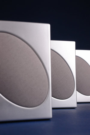 Closeup shot of three silver loudspeakers over dark blue background