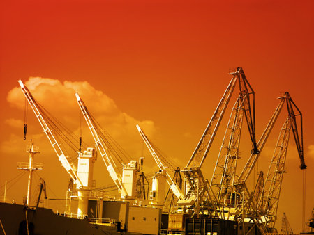Silhouettes of giant cranes at the port of transhipment against orange sky