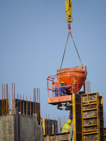 Construction worker pouring concrete mix from charging hopper platform hooked up to jib crane